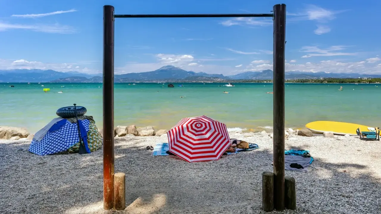 Słoneczne plaże nad jeziorem Garda, z parasolami, leżakami i wodnymi atrakcjami w tle.