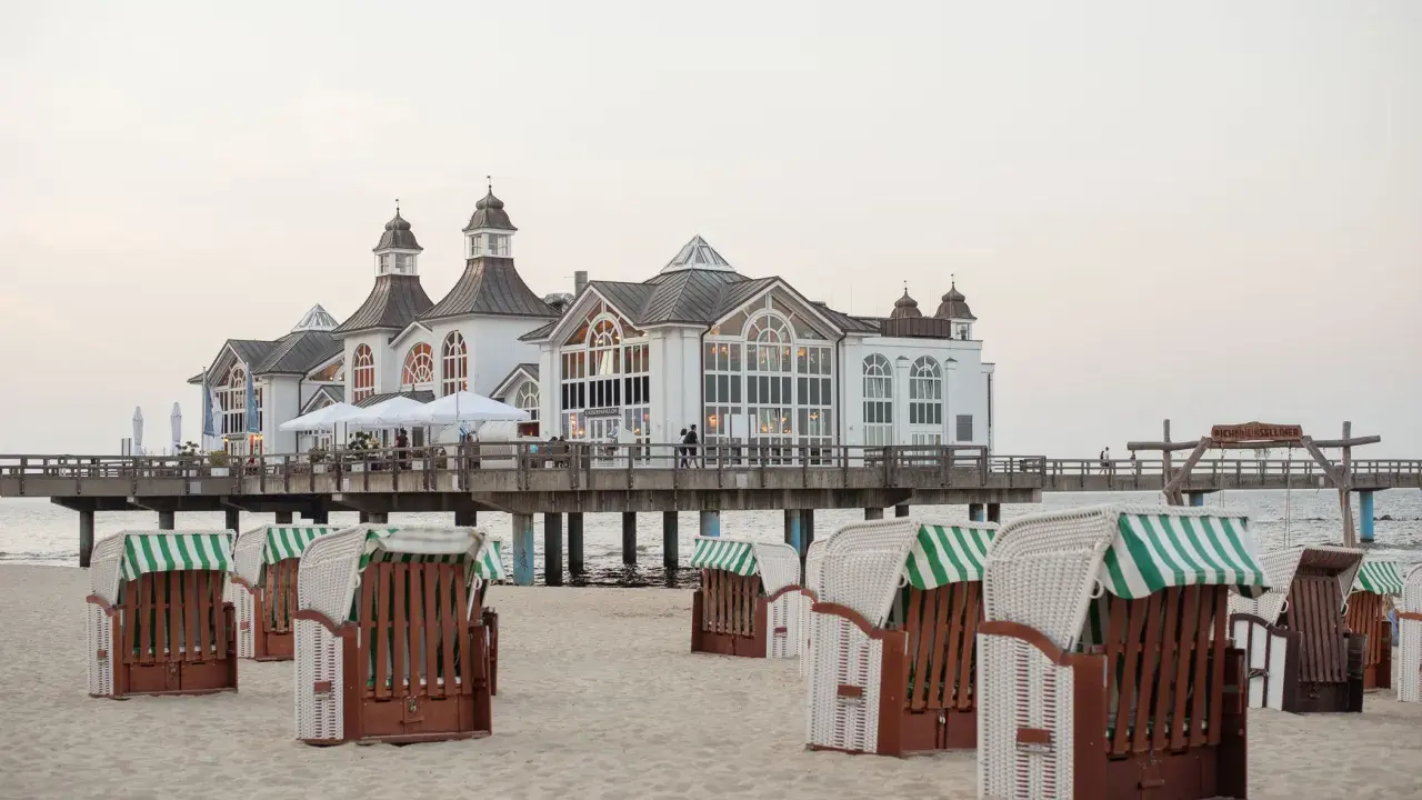 Plaża na wyspie Rugia z charakterystycznymi koszami plażowymi i molo prowadzącym do białego pawilonu.