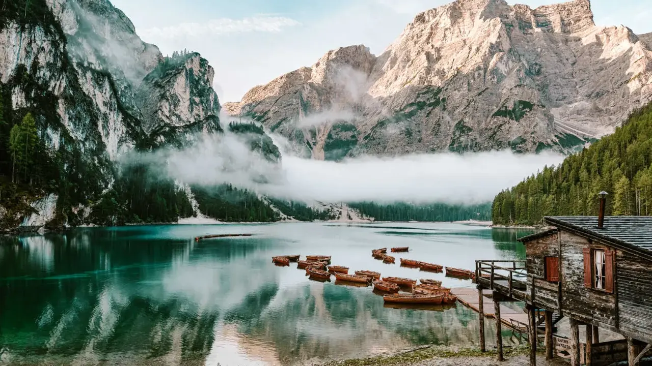 Spokojne jezioro w Dolomitach, Tyrol Włochy, z łodziami przy drewnianym molo i mgłą otulającą góry.