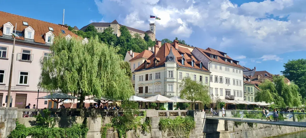 Urokliwy widok na rzekę i zabytkowe kamienice w Słowenii, Lublana. W tle widać zamek na wzgórzu.