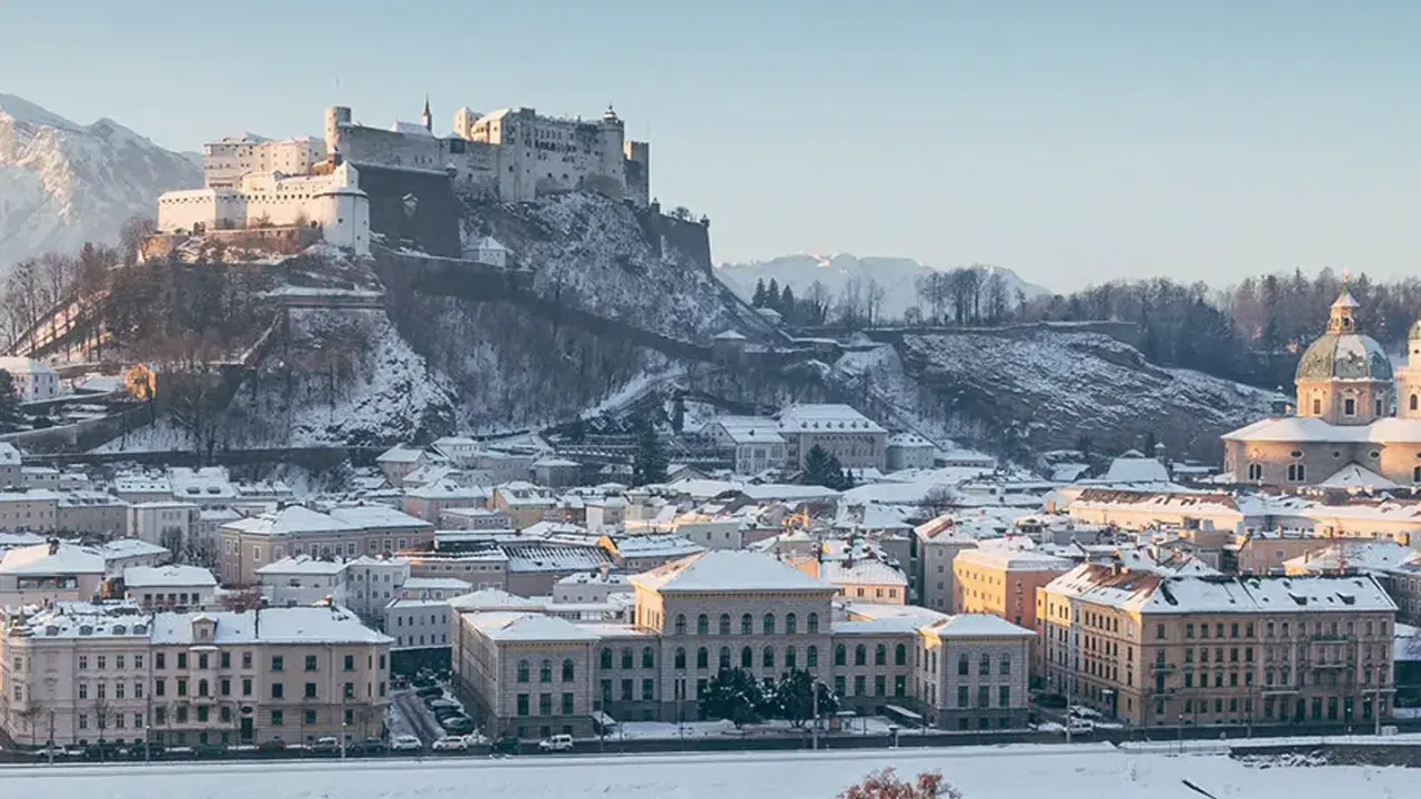 Salzburg zimą. Majestatyczna twierdza Hohensalzburg góruje nad zasypanym śniegiem miastem i rzeką Salzach.