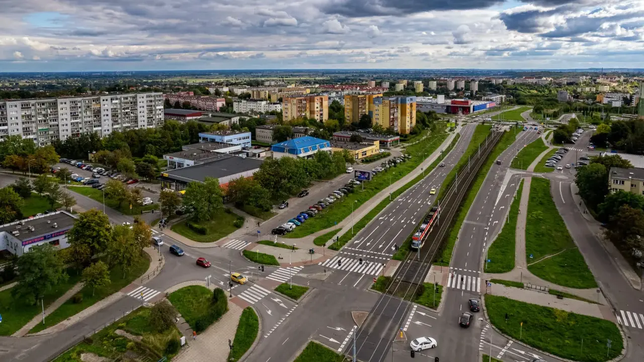 Widok z lotu ptaka na ruchliwe skrzyżowanie w Gdańsku Chełmie, z tramwajem, samochodami i budynkami mieszkalnymi w tle.