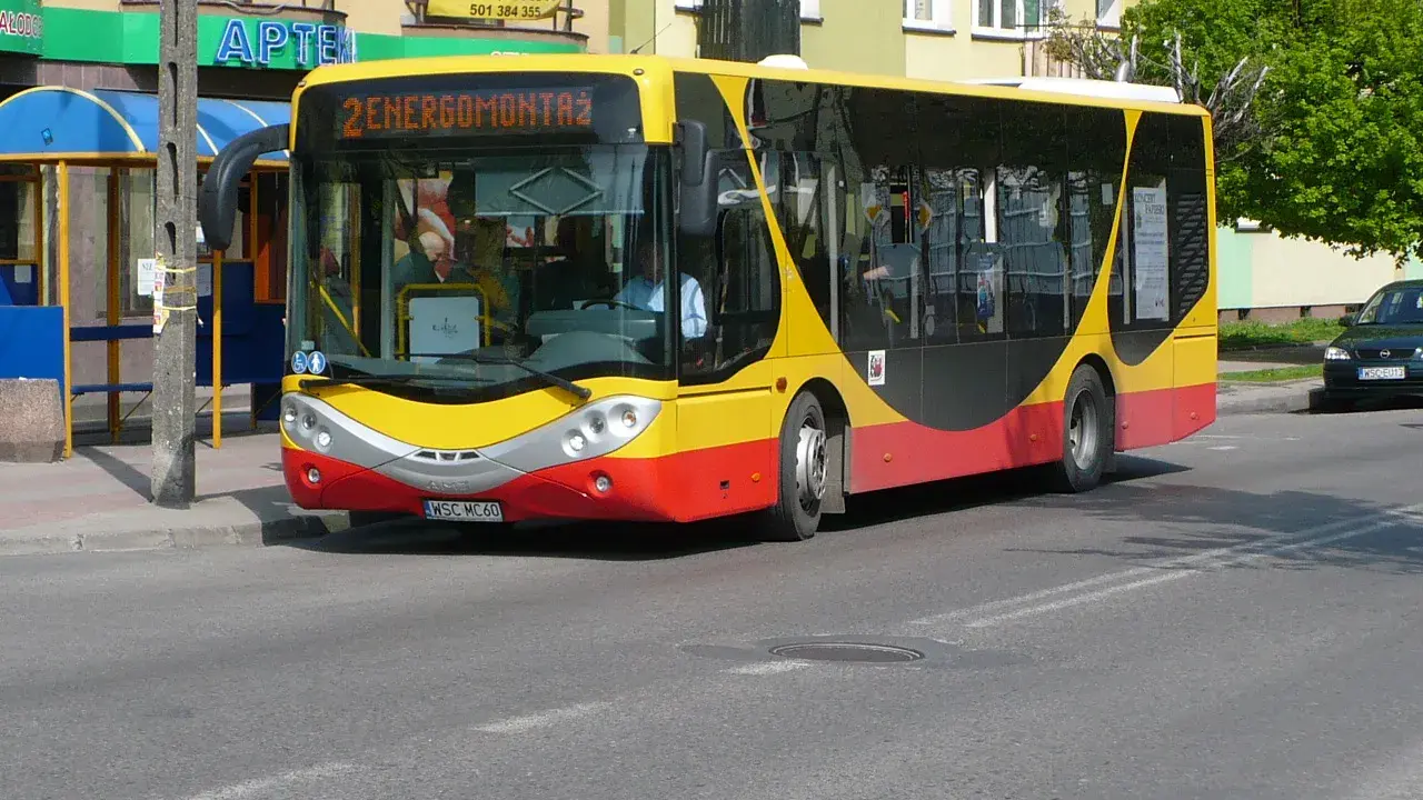 Żółto-czerwony autobus miejski z napisem "2 ENERGOMONTAŻ" na trasie w Sochaczewie.