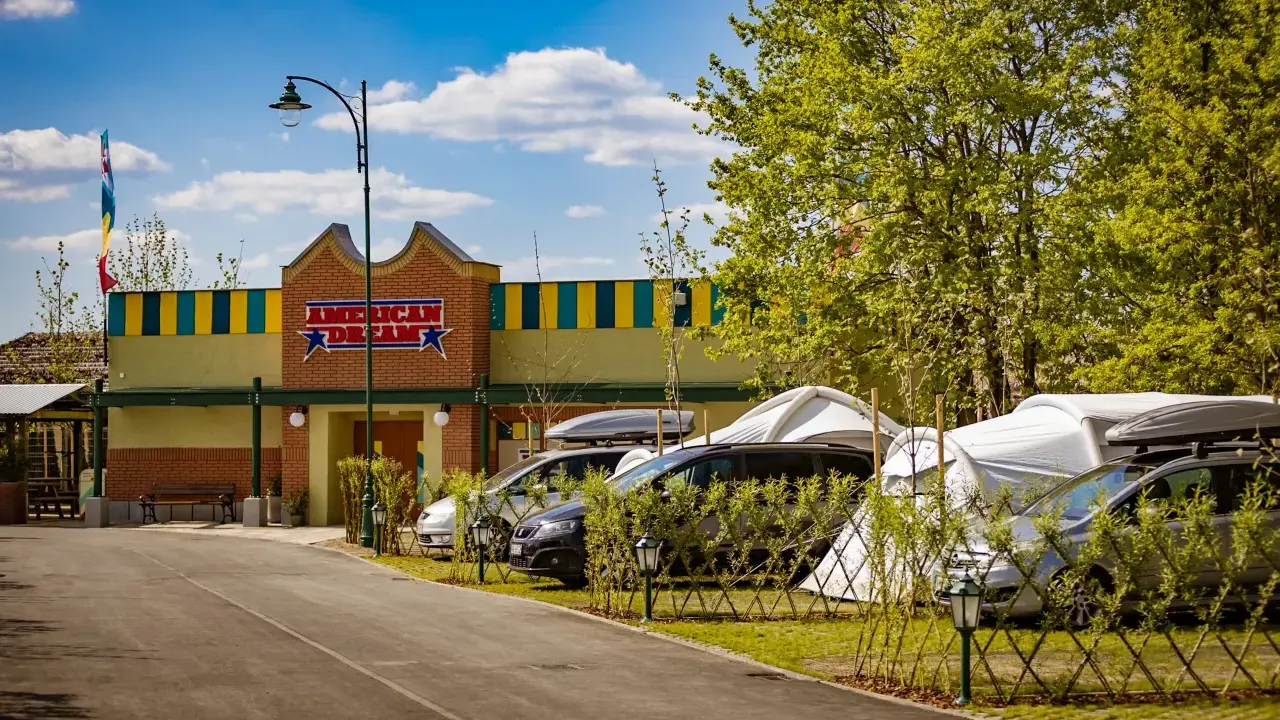 Zator Energylandia trasa: parking z samochodami i namiotami pod budynkiem "American Dream" w słoneczny dzień.
