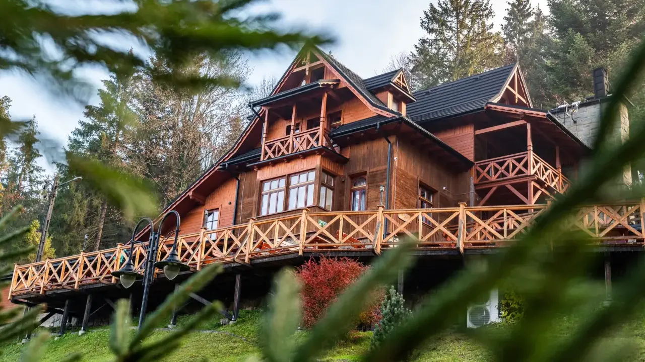 Drewniane schronisko turystyczne z tarasem i balustradą, otoczone drzewami.