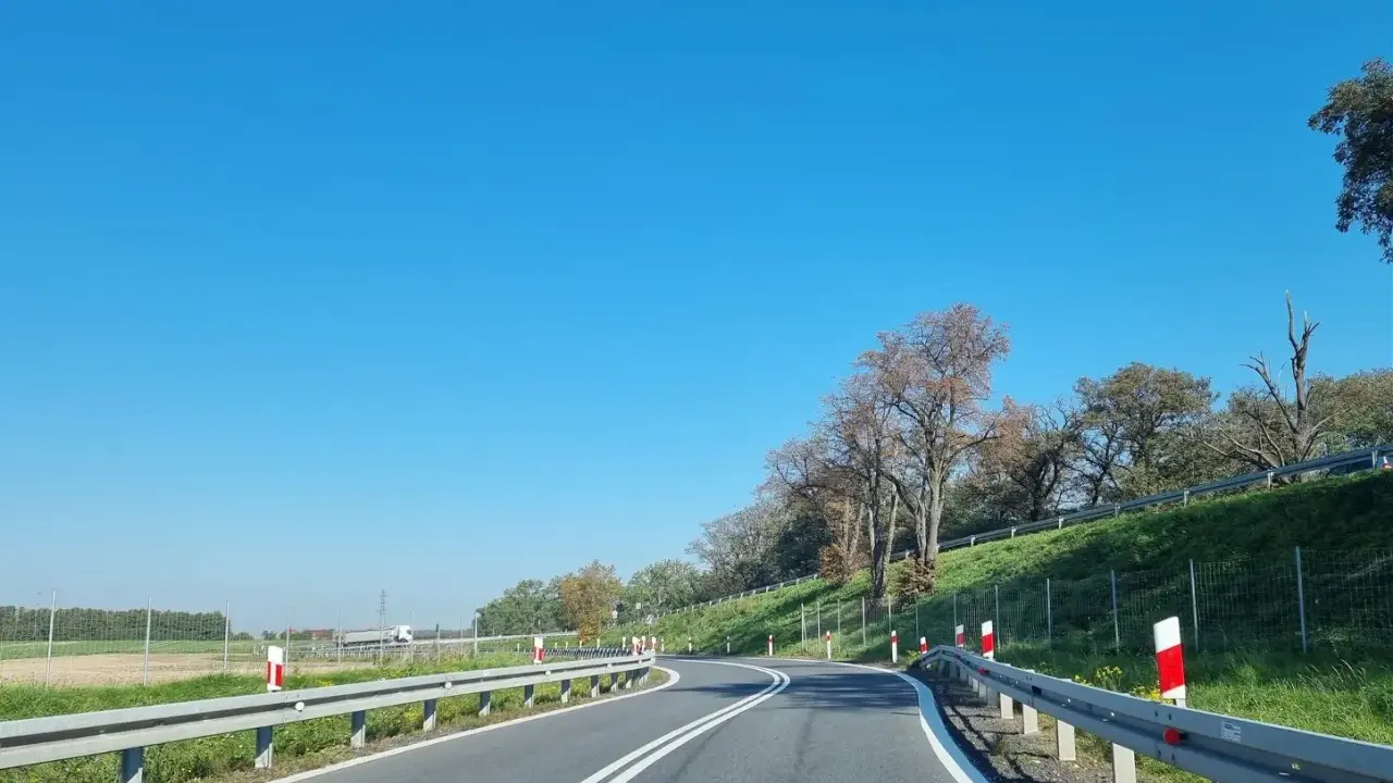 Słupki na autostradzie wyznaczają zakręt drogi. Jasne niebo i zielone pobocze tworzą malowniczy krajobraz.