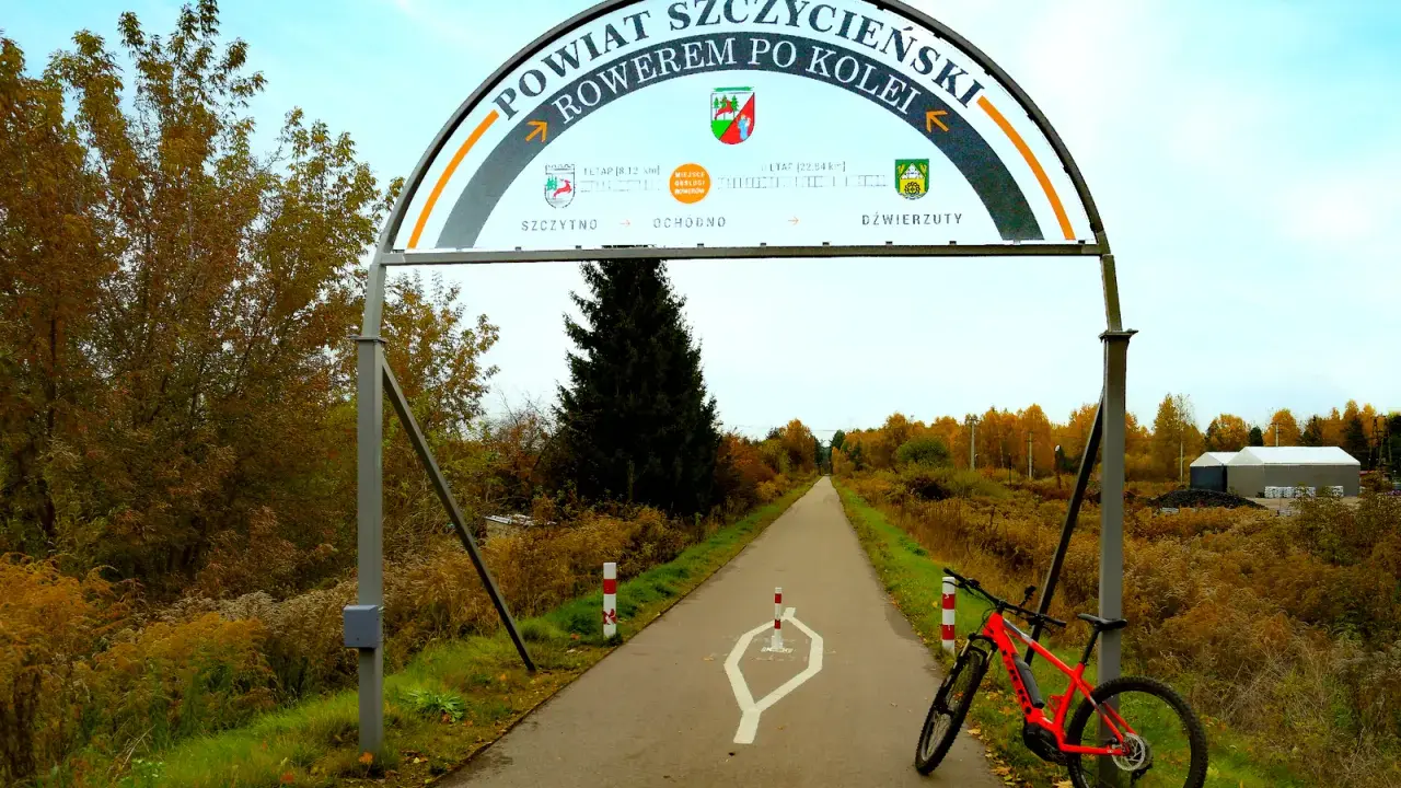 Pomarańczowy rower czeka na przygodę na trasie rowerowej w Szczytnie. Łuk nad drogą zaprasza do odkrywania powiatu.