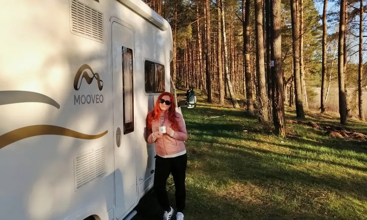 Kobieta z kubkiem kawy przy kamperze w lesie. Wspaniała przygoda z kamperem w Finlandii.