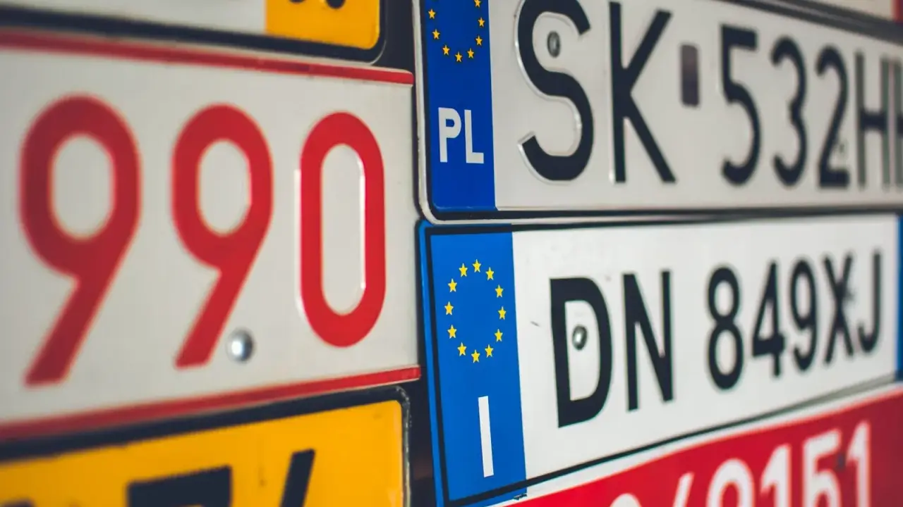 Stos tablic rejestracyjnych, w tym polskie z symbolem PL i europejską gwiazdką. Widać numery takie jak 990, SK 532HH, DN 849XJ.
