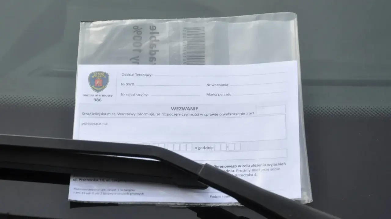Wezwanie od Straży Miejskiej za złe parkowanie. Dokument zawiera pieczęć Straży Miejskiej Warszawa, numer alarmowy 986 i pole do wpisania przyczyny wezwania.