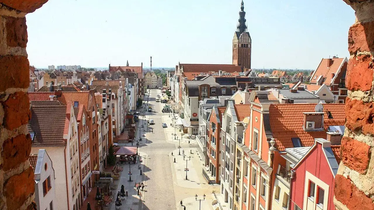 Widok na ulicę w **starym mieście Elbląg** z ceglanego muru. W oddali widać wieżę kościoła.