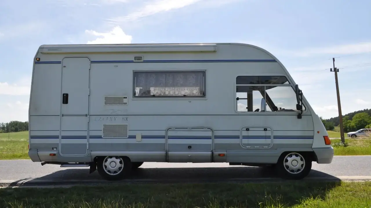 Biały ford galaxy camper z niebieskimi pasami stoi na poboczu drogi. W tle zielone pola i błękitne niebo.
