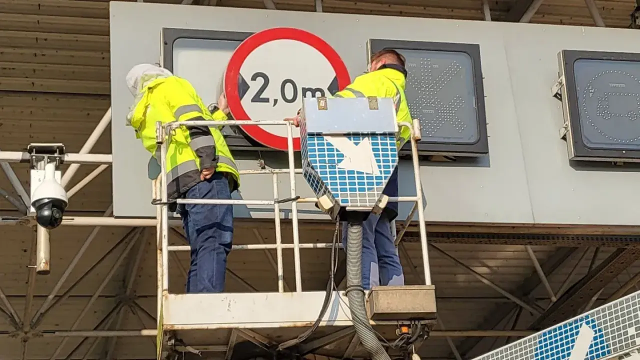 Pracownicy na podnośniku montują znak zakazu 2,0m, pokazując, jak działa e-toll.