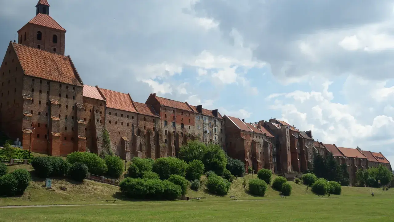 Zabytkowe miasto na trasie Ostróda-Grudziądz z ceglanymi budynkami i wieżą kościelną, otoczone zielenią i parkiem.