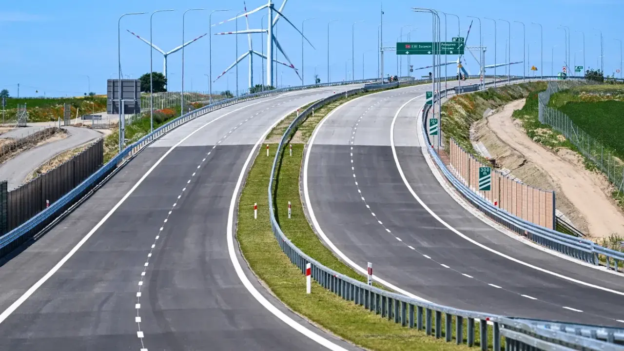 Nowa droga S6 z wiatrakami w tle. Pusta autostrada z zielonym pasem zieleni i barierami.