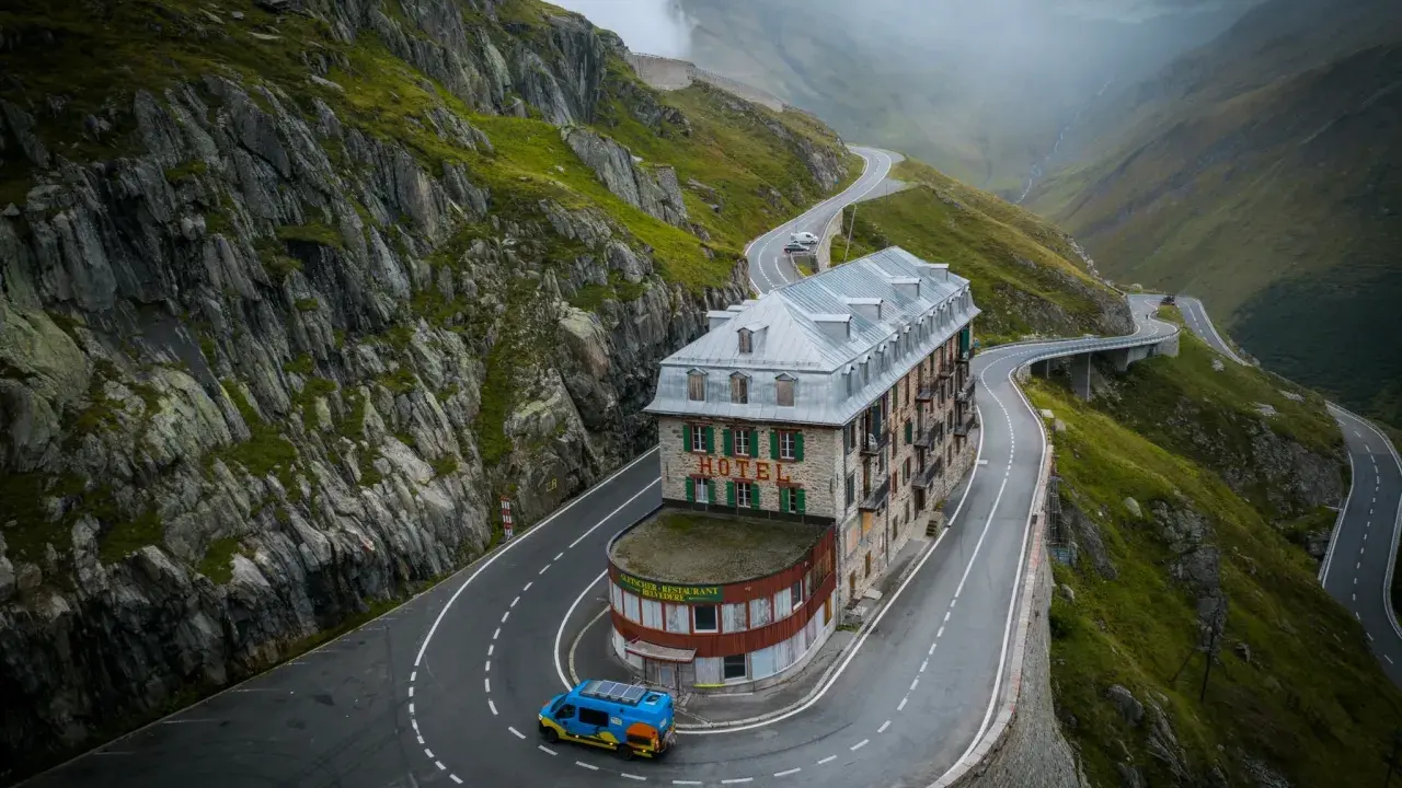 Malowniczy hotel na serpentynach w Alpach, idealny punkt na **grand tour szwajcaria**. Niebieski busik z panelami słonecznymi.