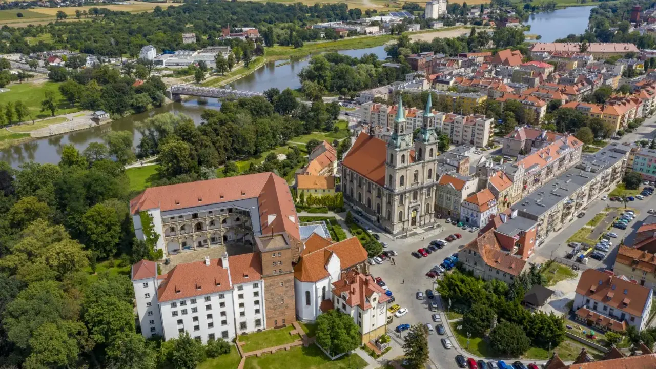 Zamek Piastów Śląskich w otoczeniu miasta i rzeki. Zabytkowa budowla z czerwonymi dachami, obok katedra z zielonymi wieżami.