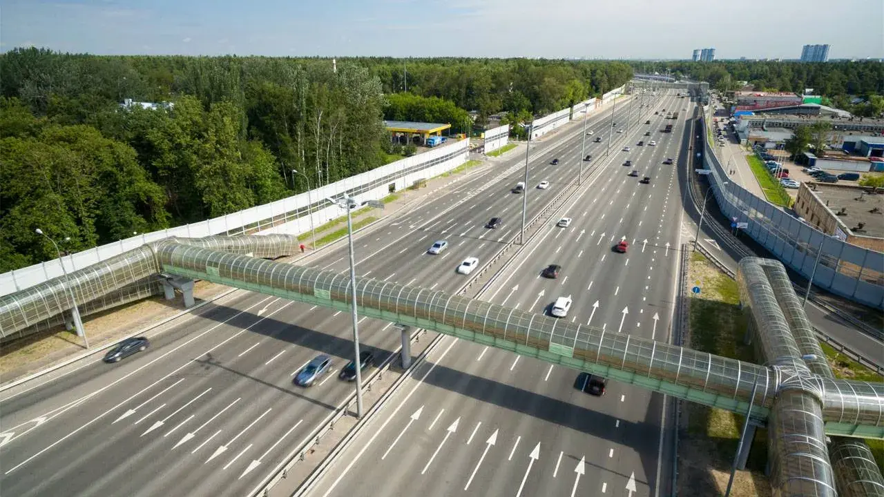 Szerokie drogi w Rosji z zielonym, przeszklonym mostem dla pieszych. Ruch samochodowy na wielopasmowej autostradzie.