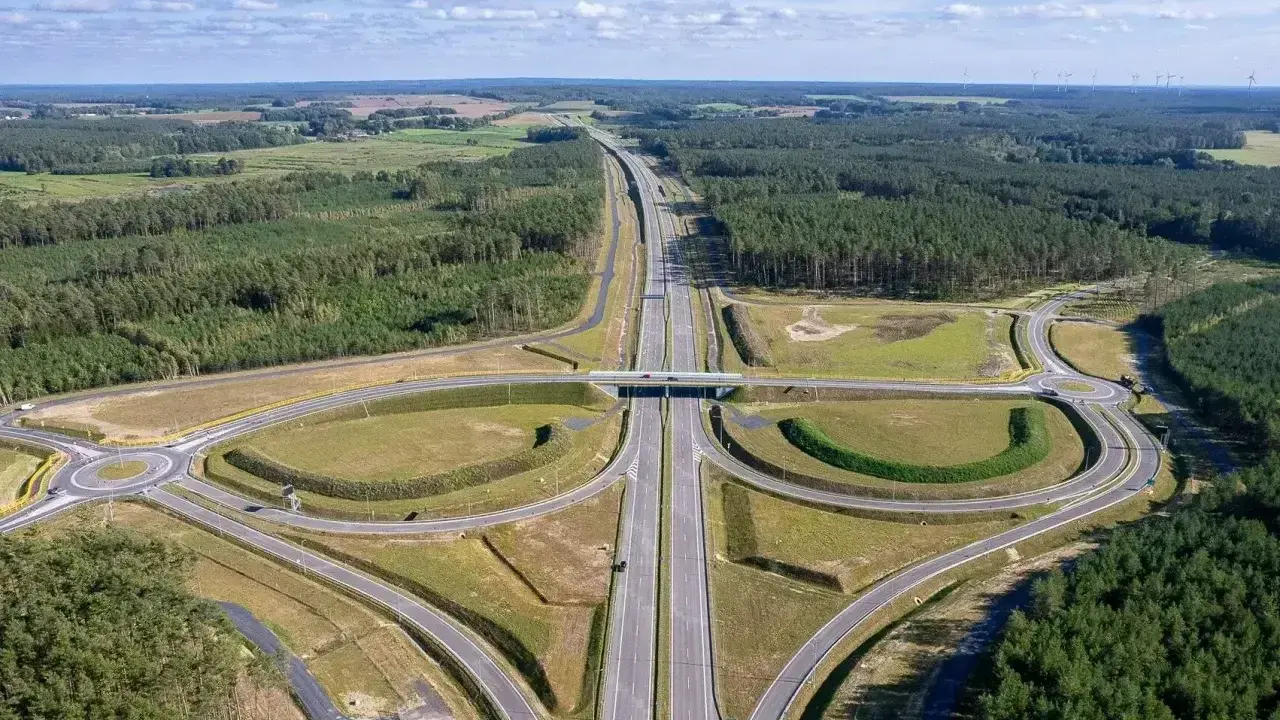 Węzeł drogowy na trasie Poznań-Kołobrzeg. Nowoczesna infrastruktura drogowa otoczona lasami i polami.