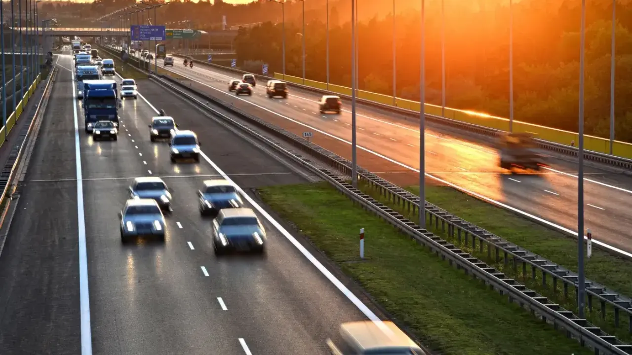 Zachód słońca nad Via Baltica. Samochody i ciężarówki pędzą autostradą w złotym blasku.