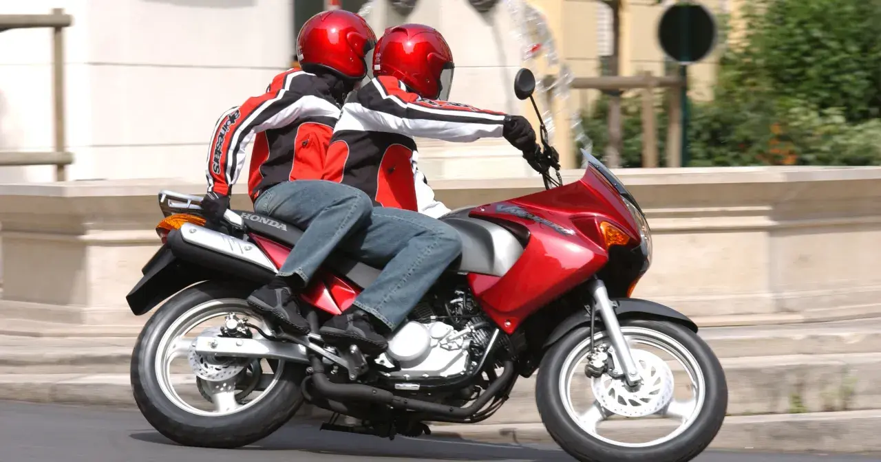 Dwie osoby w kaskach i kurtkach jadą na czerwonym motocyklu. Idealny na pierwsze prawo jazdy na 125.