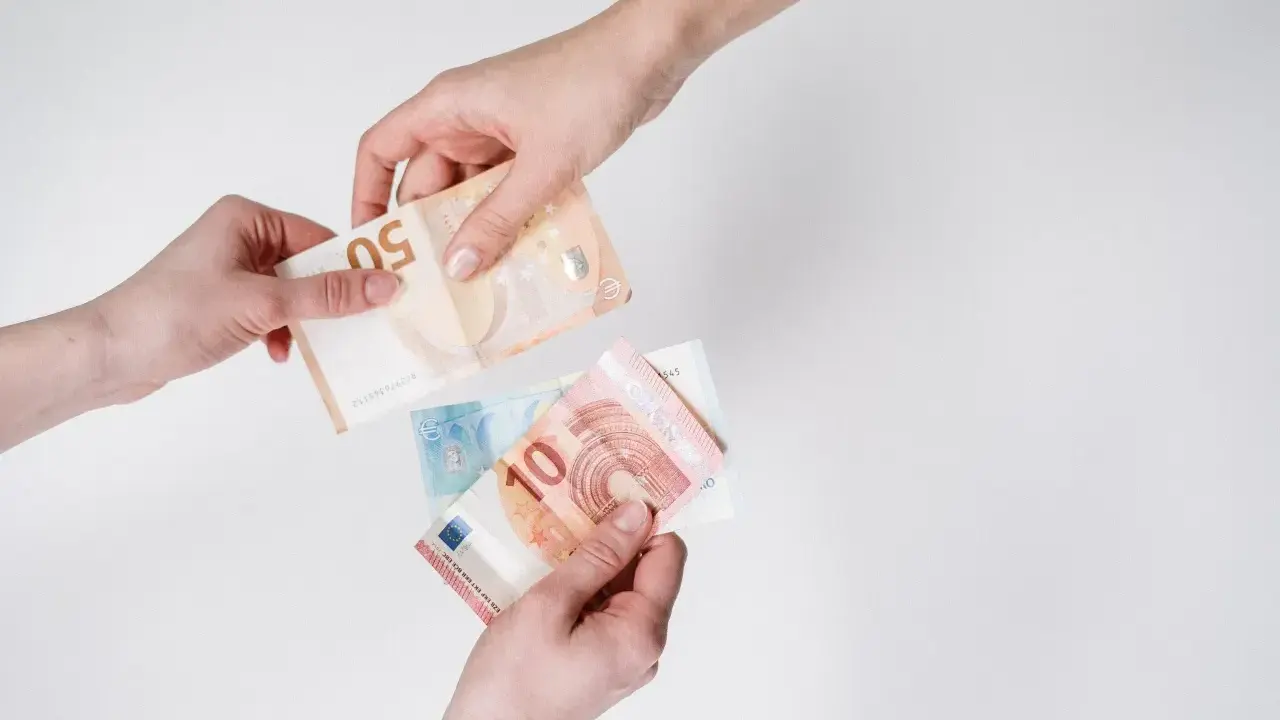 Dwie ręce przekazują sobie banknoty euro. W Austrii obowiązuje euro, co widać na przykładzie tych banknotów.