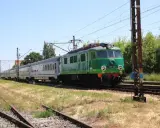 Zielony pociąg EU07-052 z wagonami mija tory w słoneczny dzień. To widok z wieluń trasa.