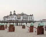 Plaża na wyspie Rugia z charakterystycznymi koszami plażowymi i molo prowadzącym do białego pawilonu.