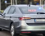 Szary, nieoznakowany radiowóz Skoda Superb z włączonymi niebieskimi światłami i napisem "POLICJA" na tylnej szybie.