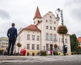 Mężczyzna stoi na rynku w Trzebnicy, podziwiając zabytkowy ratusz. Trasa spacerowa przez miasto prowadzi obok pięknych budynków.
