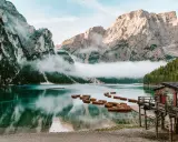 Spokojne jezioro w Dolomitach, Tyrol Włochy, z łodziami przy drewnianym molo i mgłą otulającą góry.