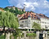 Urokliwy widok na rzekę i zabytkowe kamienice w Słowenii, Lublana. W tle widać zamek na wzgórzu.
