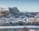 Salzburg zimą. Majestatyczna twierdza Hohensalzburg góruje nad zasypanym śniegiem miastem i rzeką Salzach.