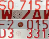 Czerwone tablice rejestracyjne z napisem "PL" wskazują na Polskę. Widoczne są numery rejestracyjne pojazdów.