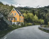 Żółty dom w Norwegii przy krętej drodze. W tle las i ośnieżone góry.