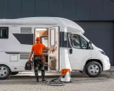 Fachowiec przygotowuje się do naprawy poszycia kampera z laminatu. W ręku trzyma narzędzia, obok stoi odkurzacz.