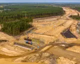 Ogromna budowa dróg w Polsce. Teren prac budowlanych z maszynami, dźwigami i przygotowywaną nawierzchnią, otoczony lasem.