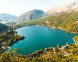 Jezioro w Abruzji, otoczone zielonymi wzgórzami i górami, z kilkoma domami na brzegu. To wspaniałe abruzja atrakcje.