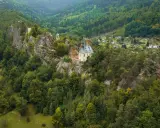 Malowniczy kościółek na skale, otoczony lasami, to jedno z **ciekawych miejsc w Czechach**. W oddali widać domki w dolinie.