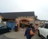 Karczma w Miłośnej, jedna z restauracji na trasie, zaprasza gości. Widać samochody i ludzi wchodzących do środka.