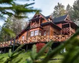 Drewniane schronisko turystyczne z tarasem i balustradą, otoczone drzewami.