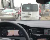Utrudnienia na drodze, korek przed budową. Samochody stoją w deszczu, nawigacja pokazuje objazd.