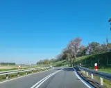 Słupki na autostradzie wyznaczają zakręt drogi. Jasne niebo i zielone pobocze tworzą malowniczy krajobraz.