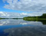 Spokojne jezioro na pojezierzu fińskim, odbijające chmury i zielone lasy.