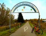 Pomarańczowy rower czeka na przygodę na trasie rowerowej w Szczytnie. Łuk nad drogą zaprasza do odkrywania powiatu.