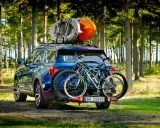 Niebieski SUV z dwoma rowerami na bagażniku i kajakami na dachu samochodu, gotowy na przygodę w lesie.