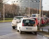 Biały Volkswagen up! zaparkowany tuż przy przejściu dla pieszych. W tle inne samochody i budynek.