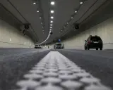 Wnętrze tunelu z samochodami i ciężarówką. Widać wyraźnie jaki odstep w tunelu między pojazdami, oświetlenie i wentylatory.