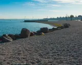 Kamienista plaża nad jeziorem, idealna na spacer po Peschiera del Garda. Widok na spokojną wodę i zarys miasta.