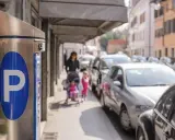 Parkomat z symbolem "P" i w tle kobieta z dziećmi na wózku, a obok samochody. Czy to parkowanie w miejscu niedozwolonym?
